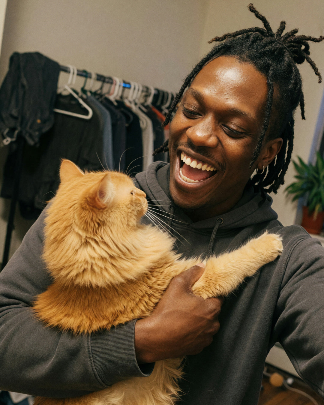 Man laughing while holding a fluffy orange cat that pushes away